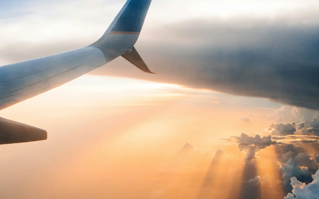 View from an airplane window showing the wing against a colorful sky with sun rays breaking through clouds at sunset.